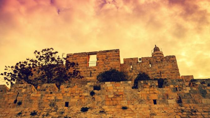 section of Old City of Jerusalem walls against orange-tinged sky 