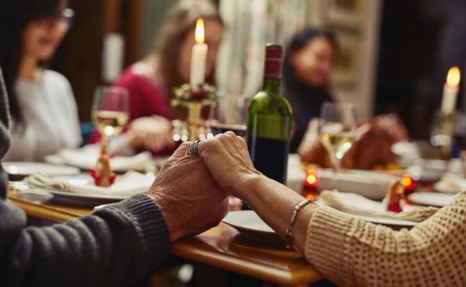 people holding hands around Shabbat table, with glasses of wine and lit candles visible