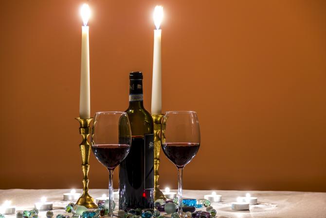 Shabbat candles, bottle of win, two wine glasses on table adorned with tea lights and decorative stones 