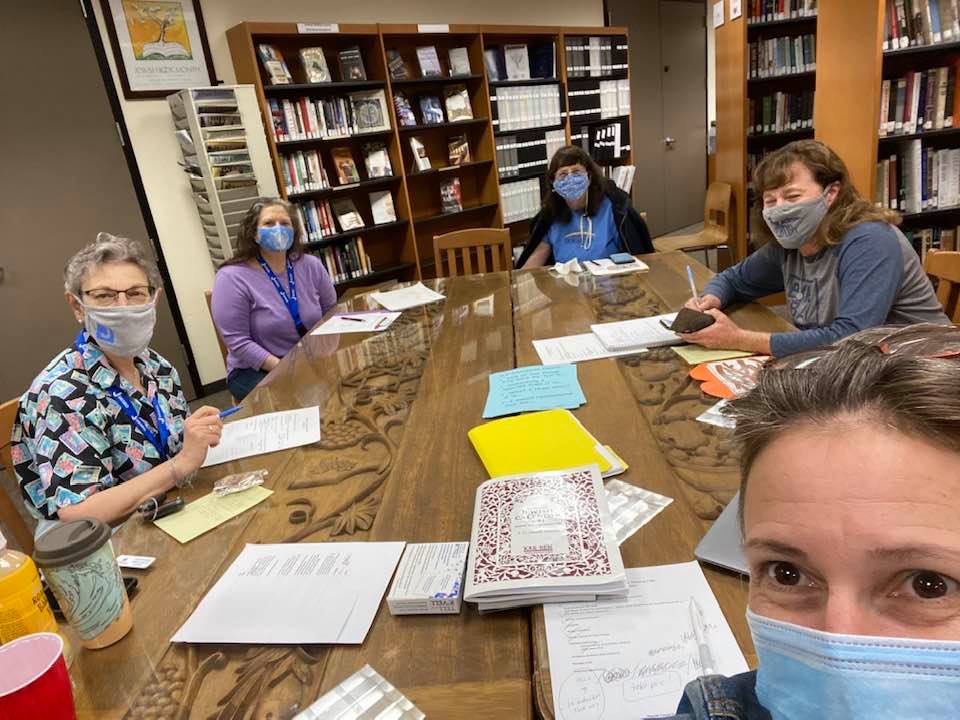 Teachers sit masked around a table in a library.