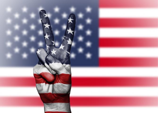 American flag projected against white background and upraised hand in a peace sign