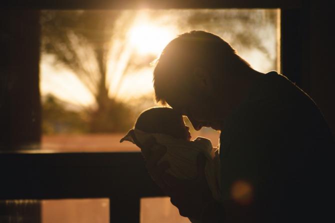 Man holding a baby in front of a rising sun