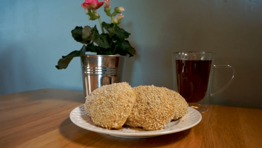 Iraqi Purim treats on a plate, with a mug of tea and a vase of flowers